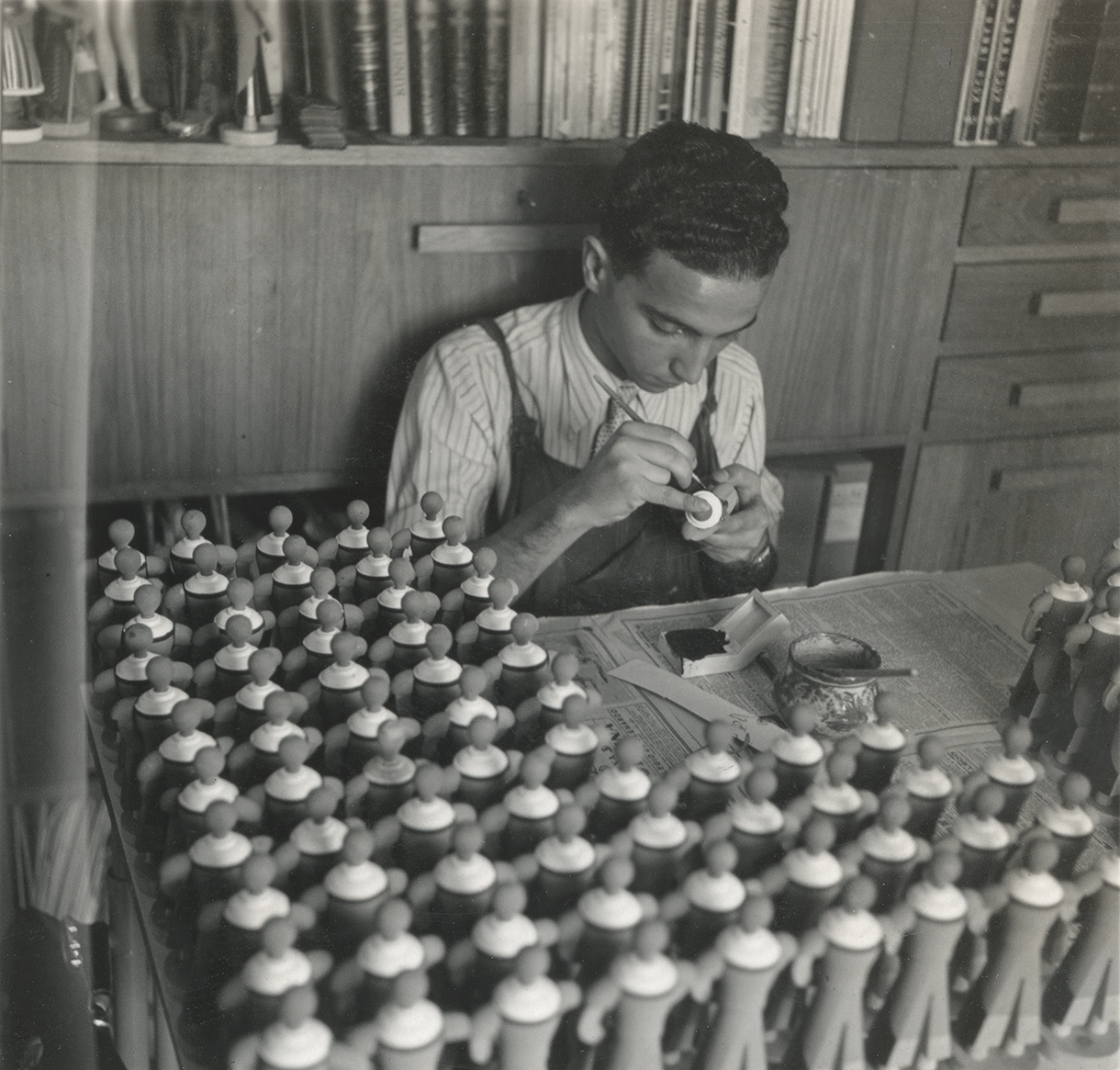 A painter at work in front of rows of unpainted wooden figures